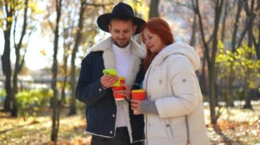 Neşeli Kafkasyalı LGBT erkeği ve olgun kadın akıllı telefon uygulamasında sosyal medyayı kaydırarak dışarıda konuşuyorlar. Olumlu oğul ve anne sohbet ediyorlar internette sonbahar parkında eğleniyorlar.