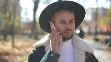 Kendine güvenen beyaz bir adamın güneş ışığında yürürken telefonla konuşmasının yakın plan resmi. Yakışıklı LGBT elemanının portresi güneş ışınlarıyla dışarıda geziniyor ve sohbet ediyor.