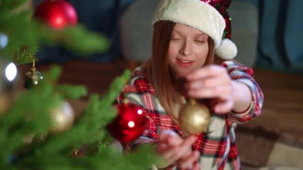 迷人的美女看着镜头 在圣诞树上挂着圣诞玩具球 欣赏着圣诞树上的装饰品 佳节前夕 心满意足的白人千禧年夫人装饰家的画像 — 图库视频影像