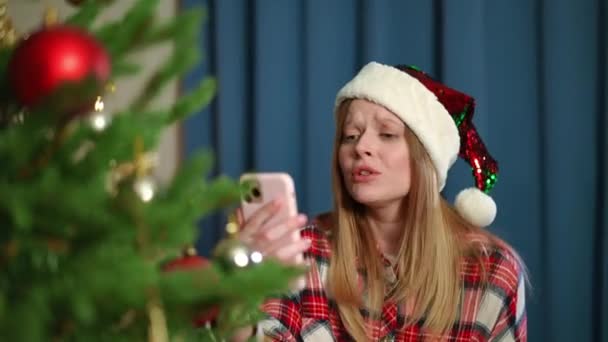 若い女性ブロガーは クリスマスツリーで屋内に立って握手指をジェスチャー話しています 大晦日にオンラインでブログ白人女性の肖像画 ホリデーシーズンとライフスタイルのコンセプト — ストック動画
