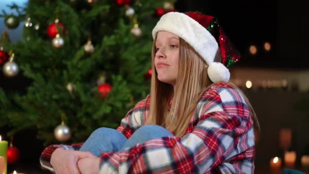 在圣诞前夕 沮丧的女人抱着膝盖坐在圣诞树旁哭泣 在家里度假的沮丧的 悲伤的高加索女人的侧角画像 — 图库视频影像