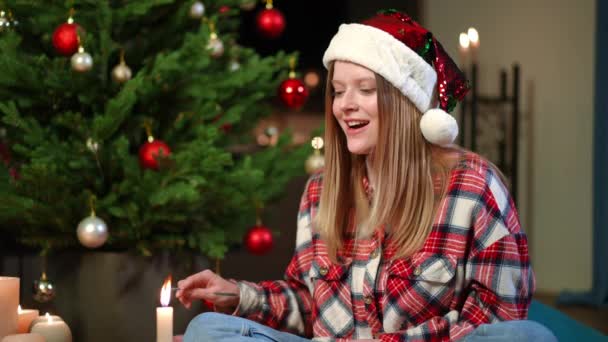 一个快乐的年轻女子用圣诞蜡烛点亮闪烁着光芒的画像 她与模糊的好奇的小狗交谈 快乐美丽的白人女士和宠物在家里共度佳节 — 图库视频影像