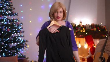 Oturma odasında kameraya bakarak şık bir elbise deneyen, ikili olmayan gülümseyen bir kadın. Beyaz ırk akışkan LGBT 'nin portresi evde Noel arifesi için hazırlanıyor.