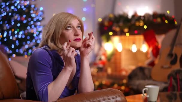 除夕之夜 白人男女同性恋 双性恋 变性者和变性者女人坐在客厅的沙发上 手指交叉 许愿闭上眼睛 希望圣诞在室内出现奇迹的性别流畅人士的画像 — 图库视频影像