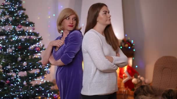 在圣诞节前夕 不满意的白人女性和年轻女性背靠背地站在室内辩论 可悲的非二元男女同性恋 双性恋和变性者在新年谈话时与朋友争吵 — 图库视频影像