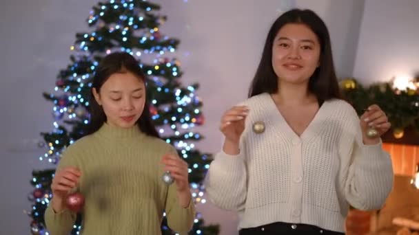 Dwie Radosne Azjatki Patrzące Aparat Uśmiechem Pokazujące Noworoczne Zabawki Stojące — Wideo stockowe