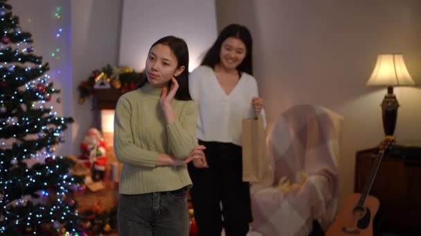 クリスマスのリビングルームに立っている若い美しいアジアの女性は ギフトで買い物袋を渡す背景から歩いて友人として前夜 新年のプレゼントに感謝を抱き興奮した女性 — ストック動画