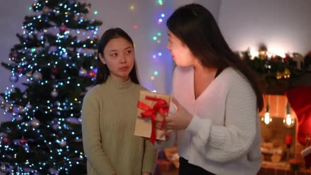 兴奋的亚洲女人展示礼品盒 里面闪烁着光芒 与讽刺的朋友交谈 站在家里客厅里的快乐女士自夸新年礼物的画像 个性和圣诞节 — 图库视频影像