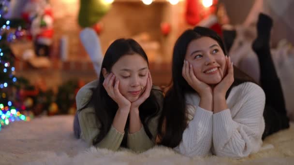 两个轻松的亚洲女性朋友在客厅里躺在柔软的地毯上谈笑风生 无忧无虑的年轻貌美女子在室内与人聊天 摇动着腿 享受着闲暇 — 图库视频影像