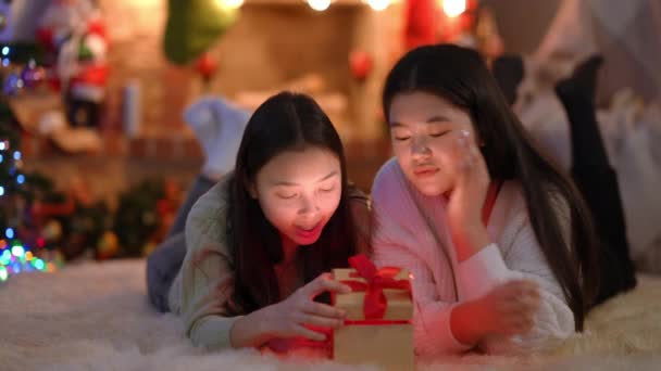 两个兴奋的亚洲女人打开礼品盒 里面闪烁着轻松的微笑 令人惊讶的年轻迷人的女性朋友们躺在客厅的地毯上享受新年的到来 — 图库视频影像