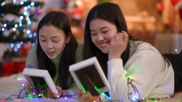 两个带着相框 头戴圣诞花环 自信放松的亚洲女人的画像 她们在地毯上谈笑风生 快乐的朋友们 在新年前夜 在室内回忆往事 怀旧概念 — 图库视频影像