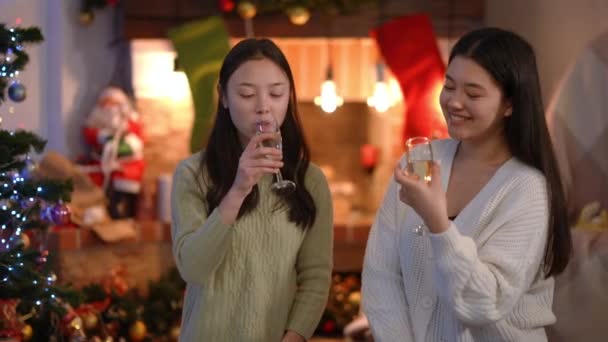 圣诞节那天 两位迷人的千年亚洲女人在室内壁炉边喝着香槟酒 微笑着聊天 积极快乐的朋友庆祝新年 — 图库视频影像