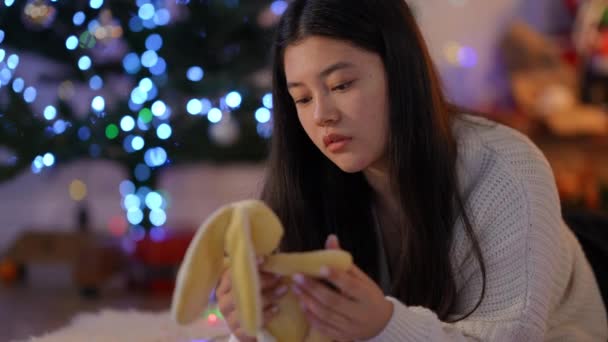 在圣诞节那天 一个人在家和玩具兔子在一起 令人沮丧而孤独的年轻亚洲女人 悲伤迷人的千禧年女子的画像 她想在孤独中度过新的一年 — 图库视频影像