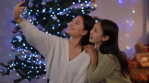 两位迷人的年轻亚洲女性在圣诞节时用智能手机应用程序在社交媒体上挥手微笑拍摄 除夕之夜 信心十足的朋友们都在屋里 祝贺和庆祝 — 图库视频影像