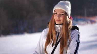 Kayak merkezinde gün ışığında durup gülümseyen ve kameraya bakan muhteşem genç bir kadın. Kafkasyalı güzel bir kadının portresi. Kışın güneşli bir havada poz veriyor. Spor ve tatiller