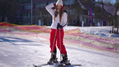 Karlı yamaçta kayak yaparken şapkasını ayarlayan geniş açılı genç bir kadın. Güneşli bir günde, kış tatilinde kayak yapan beyaz kadın portresi. Yavaş çekim