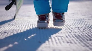 Kışlık botlu kadın ayaklarının açık havada beyaz kar üzerinde yürüdüğü yakın çekim. Tanımlanamayan, kendine güveni olan bir kadın güneşli bir günde karlı yamaçlarda geziyor.