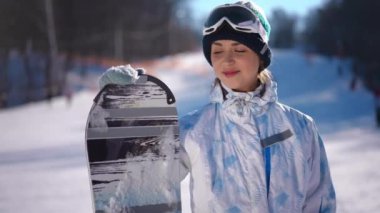 Snowboard yapan ve gülümseyen kameraya bakan muhteşem bir kadının portresi. Mutlu Kafkasyalı kadın tatillerde yavaş çekimde poz veriyor.