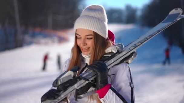 肩の上にスキーをした美しい白人女性が額で手を握りながら歩いているのを見ている 自信に満ちた豪華なスポーツ女性の肖像画は 日当たりの良い冬のスキーリゾートでゆっくりと動きます — ストック動画