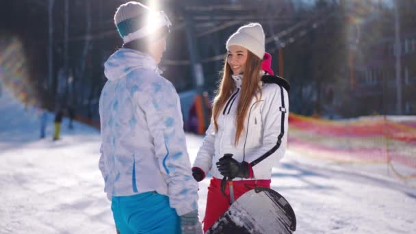 スキー場の陽射しの中に立つ2人の若い女性がゆっくりとした動きの抱擁と離れる話をする 休暇中の晴れた冬の日に満足した幸せな白人女性 — ストック動画