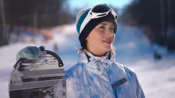 スキー場でスノーボードをしている茶色の目をしたスリムな若い白人女性は スローモーションで額に手を置いて笑っています 冬の休暇を楽しむ幸せな気楽な女性 — ストック動画