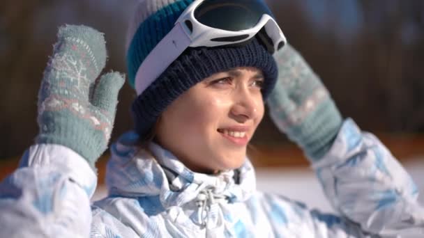年轻微笑的女人戴着滑雪板护目镜 慢吞吞地望着远方的特写 在阳光明媚的冬日度假胜地享受闲暇的白种人苗条美女的头像 — 图库视频影像