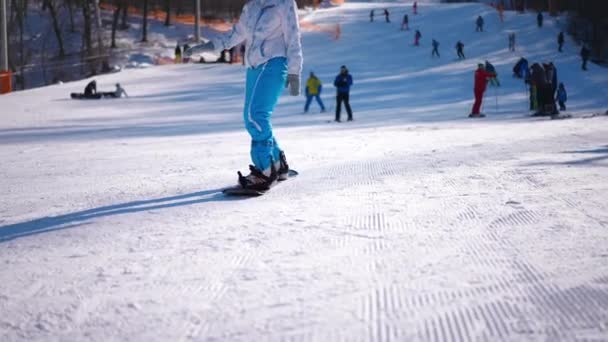 雪の斜面を残してカメラにスノーボードに乗って認識できない女性 晴れた日に屋外で冬のリゾートでレジャーを楽しむ若いフィットスポーツ女性 — ストック動画