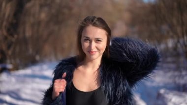 Coquette güzel beyaz kadın üstte ve kürklü açık havada güneşli bir kış gününde yavaş çekimde poz veriyor. Kahverengi gözlü, kendine güvenen esmer kadının portresi gülümseyen kameraya bakıyor.