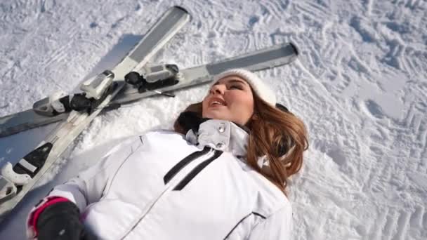 満足して屈託のない美しい女性の高角度ビューの肖像白雪の上にスキー笑みを浮かべて横たわっ 晴れた日には屋外リゾートで冬の休暇を楽しむ幸せなリラックスした白人女性 — ストック動画