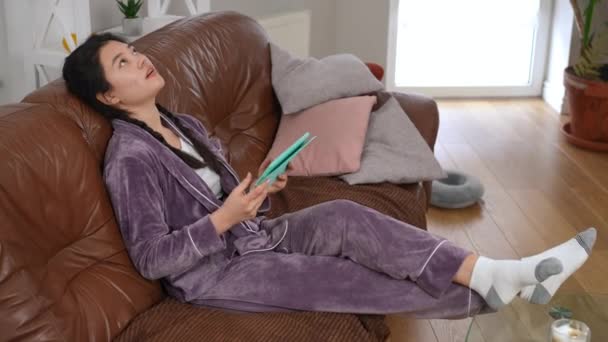 Aborrecido Asiático Bela Jovem Com Tablet Digital Pijama Sentado Sofá — Vídeo de Stock