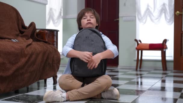 悲伤压抑的白人学童抱着背包坐在房屋走廊地板上的全景肖像 放学后在家里思考的孩子很不高兴 — 图库视频影像