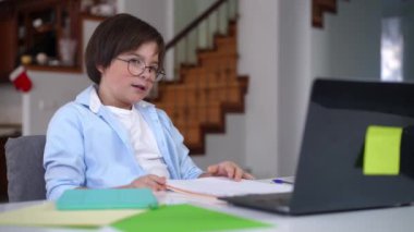 Evde dizüstü bilgisayarıyla oturmuş gülümseyen sevimli akıllı çocuk. Gözlüklü beyaz, zeki okul çocuğu içeride ders çalışıyor. E-eğitim kavramı