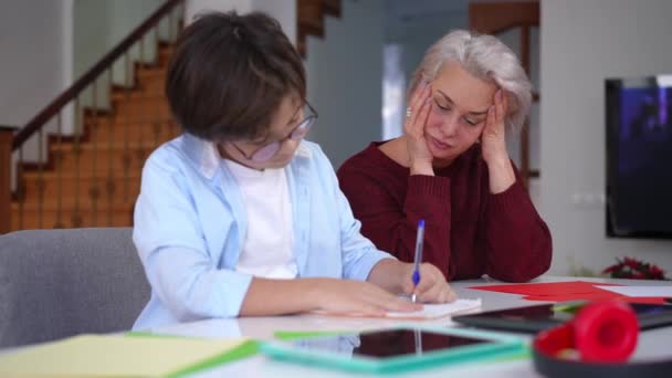 怒った男子生徒が不満そうな表情で話すペンを放り投げながら手をつないでいる圧倒的な熟女 疲れ母の肖像とともに息子が宿題をする — ストック動画