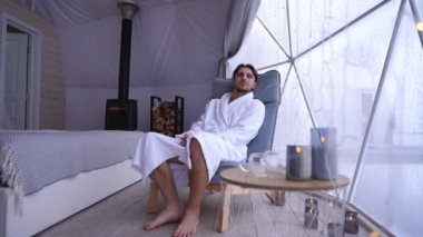 Rahatlamış bir adam yatak odasında oturmuş havluyla banyodan çıkan bir kadın gibi pencereden dışarı bakıyor. Kafkasyalı genç bir çift evde gülüşerek flört ediyor.