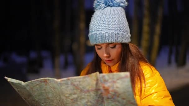 瘦小美丽的高加索女人的画像 她站在户外用纸质地图选择路线 在冬日的森林里 夜夜环顾四周 厌恶着不确定迷人的女性游客 — 图库视频影像