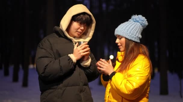 冬の夜 森の中でマグカップからお茶を飲む話をするリラックスした正のカップル アジアの若者と白人女性が屋外でチャットキャンプをハイキング — ストック動画
