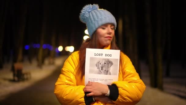 冬の夜に野外を見回して立っている迷子の犬の発表を持つ欲求不満若い女性 悲しい落ち込んでいる白人女性の肖像 ペットを探している街の通り — ストック動画
