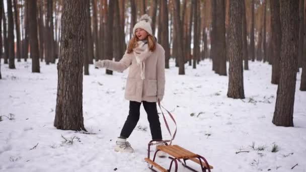 在冬天的森林里 一个快乐的女孩站在雪橇上跳舞 她的全景像在歌唱 积极快乐的白人青少年在户外公园度假的乐趣 — 图库视频影像