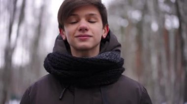 Kendine güvenen beyaz çocuk kumral saçlarını düzeltiyor ve kahverengi gözleriyle kameraya bakıyor. Kendine güvenen genç turistin portresi. Kış ormanlarında gülümseyerek poz veriyor.