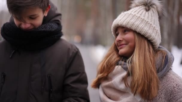 放大图片中的笑容可亲的少女和男朋友在户外约会 男朋友慢动作地把棒棒糖递给女朋友 在冬季公园聊天的白人青少年夫妇 — 图库视频影像