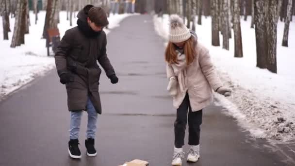 公園の路地に落ちた本を集める少女を助ける10代の少年を愛する 学校の後の冬の日に屋外で十代の白人カップルの広いショットの肖像画 — ストック動画
