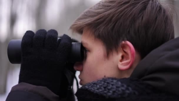 侧视特写集中的十几岁男孩望向远方用双筒望远镜 库里奥斯关注的焦点是站在室外冬季森林里享受生态旅游的白人青少年 — 图库视频影像