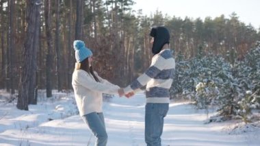 Kış ormanlarında karlı yolda ağır çekimde el ele tutuşan neşeli genç turistler. Mutlu, heyecanlı, beyaz erkek arkadaş ve kız arkadaş tatilde dışarıda eğleniyor.