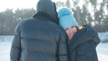 Rahatlamış gülümseyen kadın portresini yakınlaştırın. Kameraya bakın. Açık havada erkeğin yanında, güneş ışığında. Kafkasyalı genç kadının kocası yavaş çekimde poz verirken kış tatilinin keyfini çıkarması dileğiyle.