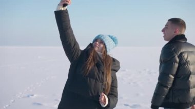 Dışarıda karlı çayırlar üzerinde duran seyyar şebeke sinyalini arayan beyaz bir çiftin orta boy fotoğrafı. Erkek ve kadın seyahatlerde düşünürken konuşuyor.