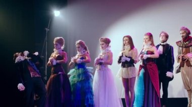 Profesyonel aktörler ve ciddi yüz ifadesi olan aktrisler tiyatro sahnesinde kostümlü performans sergilerken başroldeki adam tekerteker tekrar şarkı söylüyor. Yetenekli topluluğun kapalı mekanda gösterimi