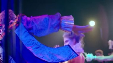 Arkadan bakıldığında, eski mavi kostümlü tanınmayan bir aktör arka planda hızla dans eden aktrisler gibi yavaş hareket ediyor. Profesyonel yetenekli beyaz erkek ve kadınlar modern peri masalı oynuyorlar.