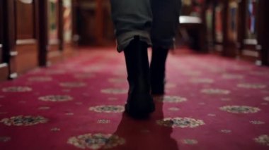 Kırmızı halıda eski moda otel koridorlarında yürüyen kadın ayaklarının izini sürüyorum. Arka planda tanınmayan genç bir kadın tatil köyünde geziniyor.