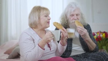 Gülümseyen yaşlı adam ve kadın kruvasan yiyor sabahları evde kahve içiyor ve konuşuyorlar. Kendine güveni tam, Kafkasyalı karı koca yavaş çekimde yemek ve içkinin tadını çıkarıyor.