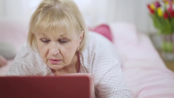 Nternette Dizüstü Bilgisayarda Pijamalarıyla Evde Yatan Konsantre Olmuş Yaşlı Kadın — Stok video